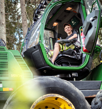 Ung kille tittar ner mot fotografen sittande i en grön stor traktor.