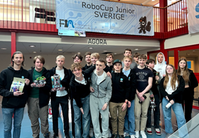 En grupp med ungdomar stående framför en trappestrad med tygskylt "Robocup för juniorer".